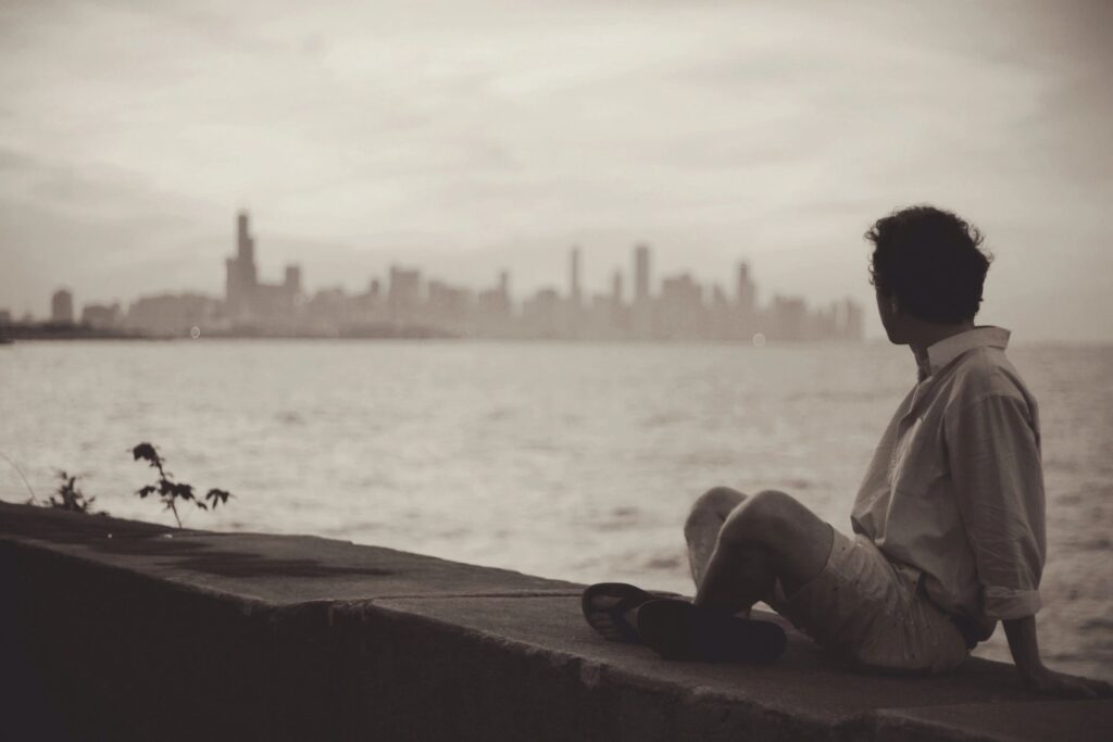 Man sitting by the waterfront, contemplating life and forgiveness after overcoming addiction.